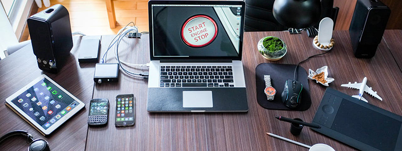 A picture of a laptop, cable chords, a phone and mouse on a desk